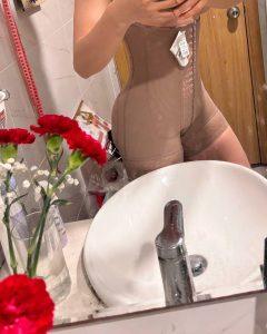 Người mặc bodysuit định hình toàn thân Ann Chery màu nude, cài móc phía trước, hỗ trợ phục hồi vóc dáng sau phẫu thuật hút mỡ – chụp qua gương trong nhà tắm, không lộ mặt.